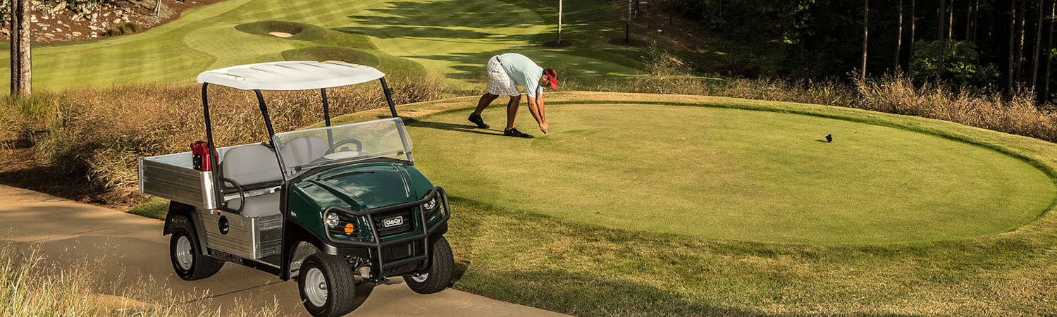 A man maintenances the golfing green with his golf car parked on the fairway.